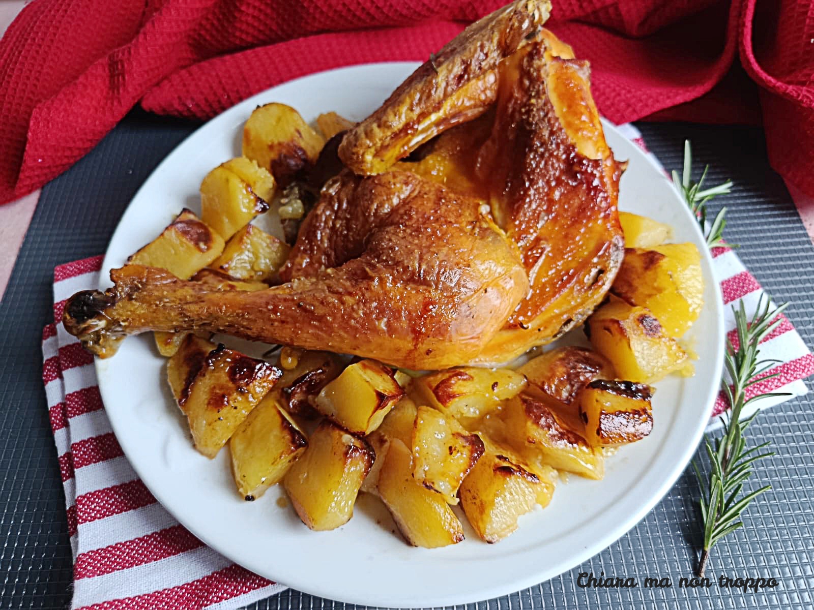 Mezzo pollo arrosto dorato e croccante in teglia, circondato da patate a spicchi rosolate, rametti di rosmarino e spicchi d'aglio