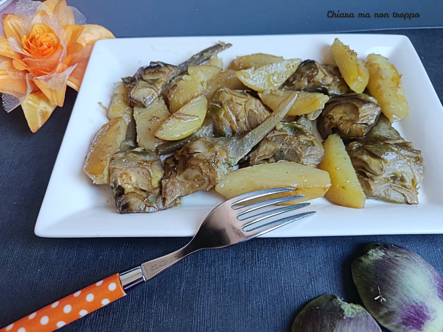Piatto rettangolare bianco con carciofi e patate a spicchi cucinati in umido, servito con una forchetta dal manico a pois su un piano scuro