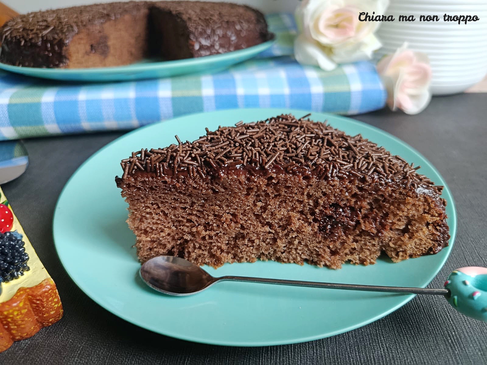 Primo piano di una fetta di torta al cioccolato, soffice su un piatto, con buchi riempiti di ganache al cioccolato fondente e decorata con codette.