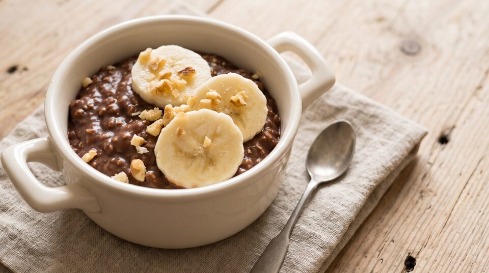 Porridge cremoso al cioccolato in una ciotola con rondelle di banana e noci spezzettate