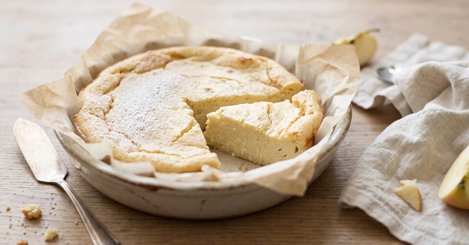 Tortino di mele e ricotta cremoso in una pirofila con una fetta tagliata e zucchero a velo