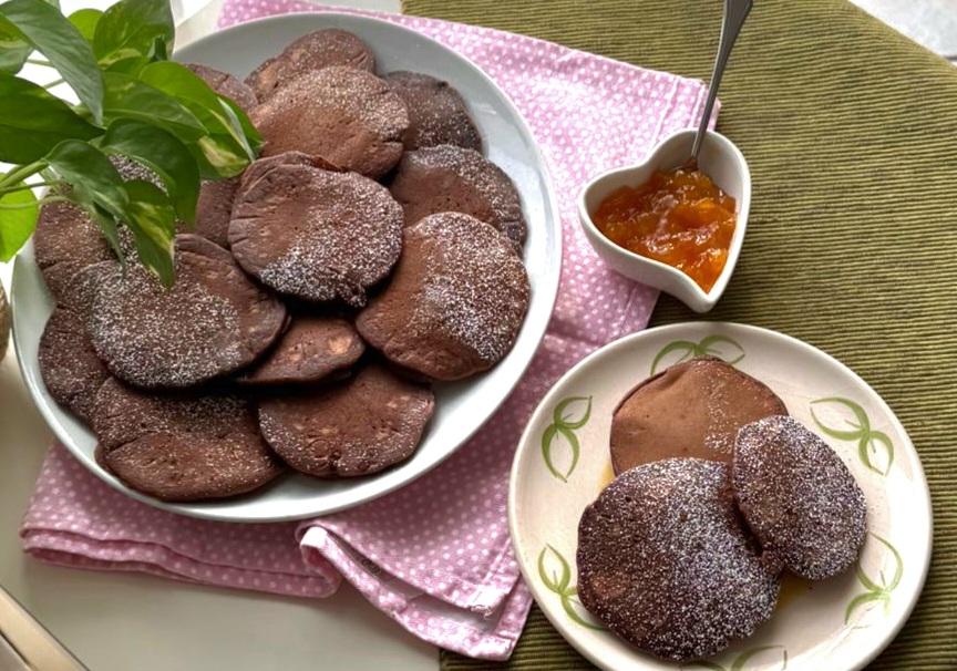 Pancakes soffici al cacao impilati per colazione con confettura a fianco coperti con zucchero a velo